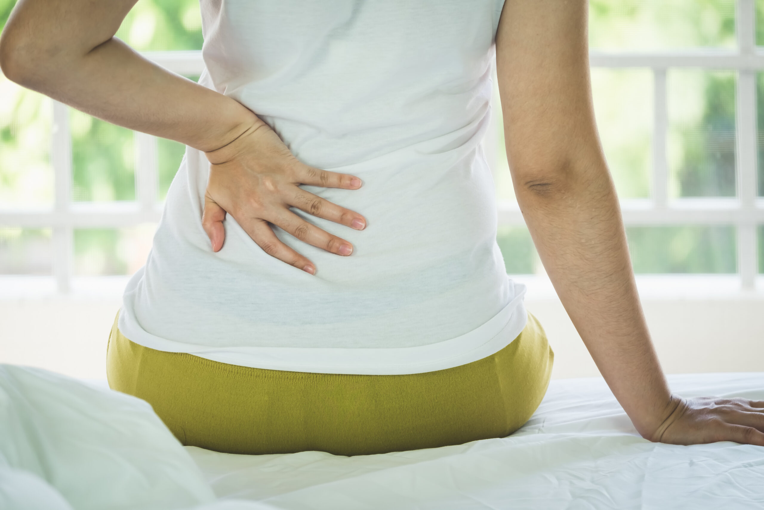 Closeup of young woman suffering from pain kidney disease while sitting on bed at home, Healthcare And Medicine concept